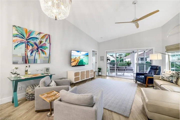 Living room featuring light wood finished floors, baseboards, high vaulted ceiling, and ceiling fan with notable chandelier