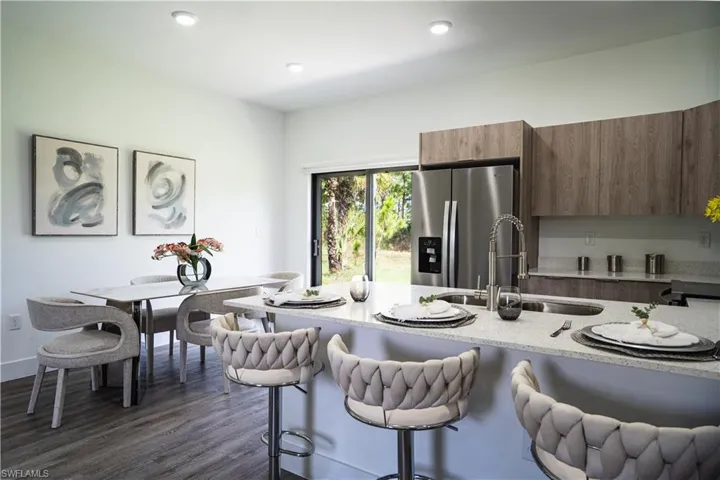 Kitchen featuring modern cabinets, stainless steel fridge, light stone counters, a breakfast bar, and wood finish cabinetry