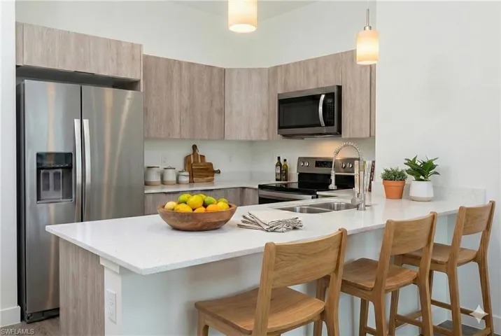 Kitchen with stainless steel appliances, a breakfast bar area, decorative light fixtures, and a peninsula **photo has been virtually staged