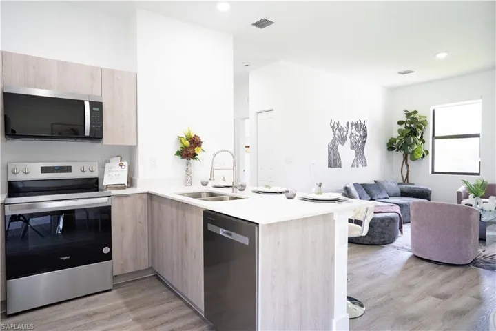 Kitchen featuring light wood finish cabinets, stainless steel appliances, a peninsula, light stone countertops, and open floor plan