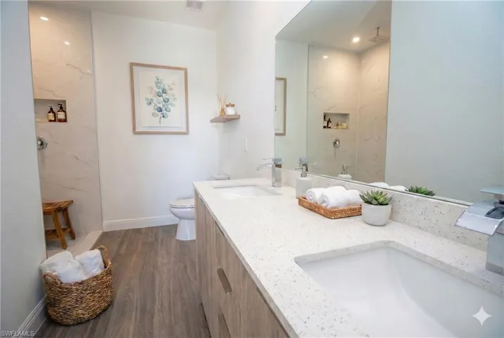 Full bathroom featuring a marble finish shower, dark wood finished floors, and double vanity  **photo has been virtually staged