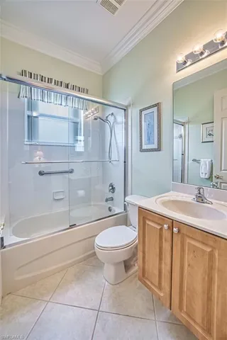Bathroom featuring combined bath / shower with glass door, vanity, ornamental molding, and light tile patterned floors