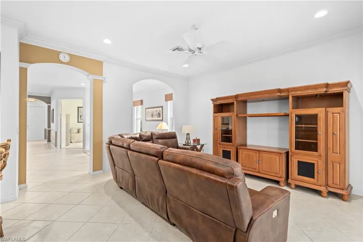 Kitchen featuring arched walkways, decorative backsplash, a kitchen bar, light stone countertops, and crown molding