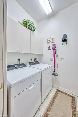 Laundry area with light tile patterned flooring, washing machine and dryer, and cabinet space