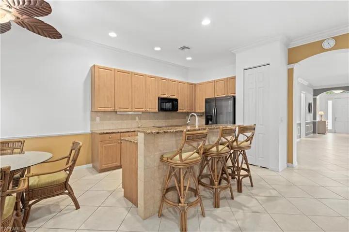 Kitchen featuring a kitchen breakfast bar, crown molding, light stone counters, tasteful backsplash, and light tile patterned floors