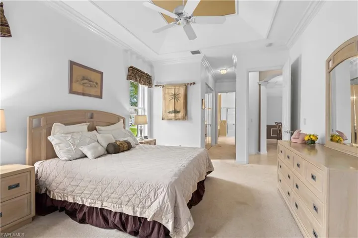 Carpeted bedroom featuring ornamental molding, ceiling fan, and a raised ceiling
