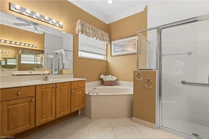 Bedroom with light colored carpet, ornamental molding, a raised ceiling, a ceiling fan, and connected bathroom