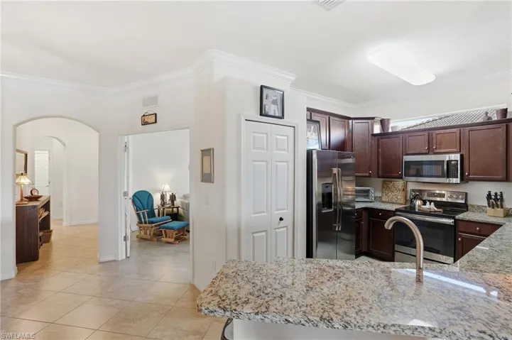 Kitchen with stainless steel appliances, light stone countertops, arched walkways, dark brown cabinets, and crown molding
