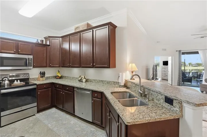 Kitchen with appliances with stainless steel finishes, a peninsula, healthy amount of natural light, light stone counters, and ornamental molding