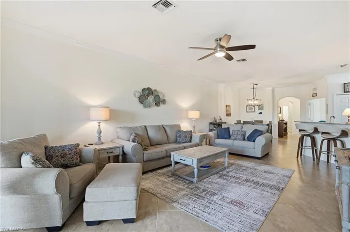 Living area featuring arched walkways, ceiling fan, crown molding, light tile patterned floors, and a chandelier