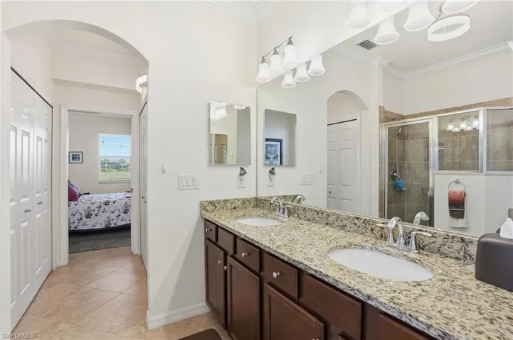 Bathroom featuring double vanity, ornamental molding, a stall shower, a closet, and light tile patterned floors