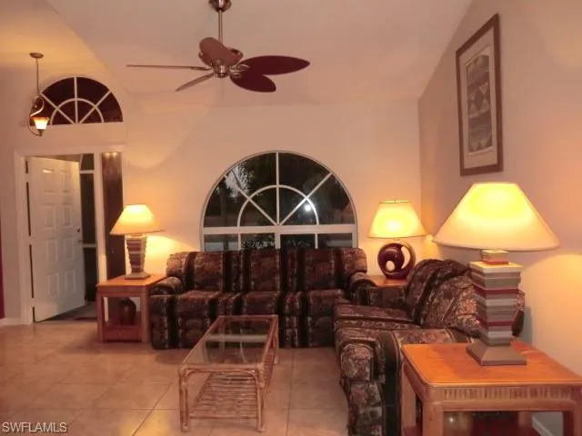 Living area featuring tile flooring, vaulted ceilings, and an arched window with decorative grilles