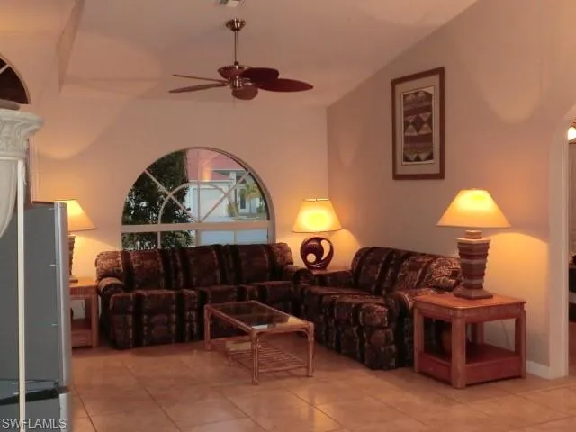 Living area featuring a vaulted ceiling with a ceiling fan, a large arched window, and tile flooring