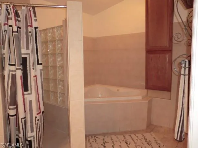 Corner soaking tub with tiled surround, adjacent to a shower enclosure with glass block wall, and upper wood-finish cabinetry