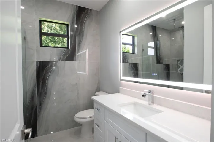 Bathroom with toilet, a tile shower, and vanity