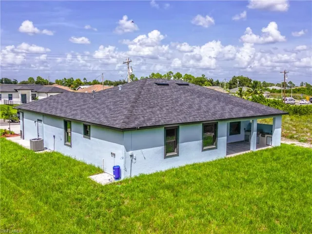 Rear view of property featuring central AC unit, a lawn, and a patio