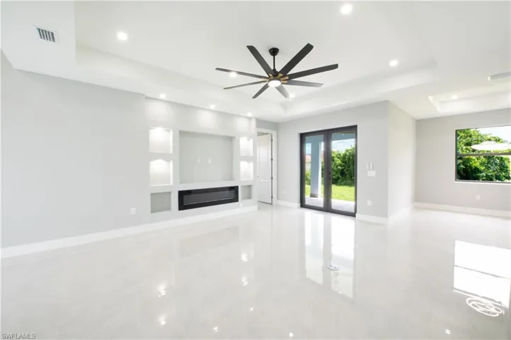 Unfurnished living room featuring a healthy amount of sunlight, ceiling fan, and a raised ceiling