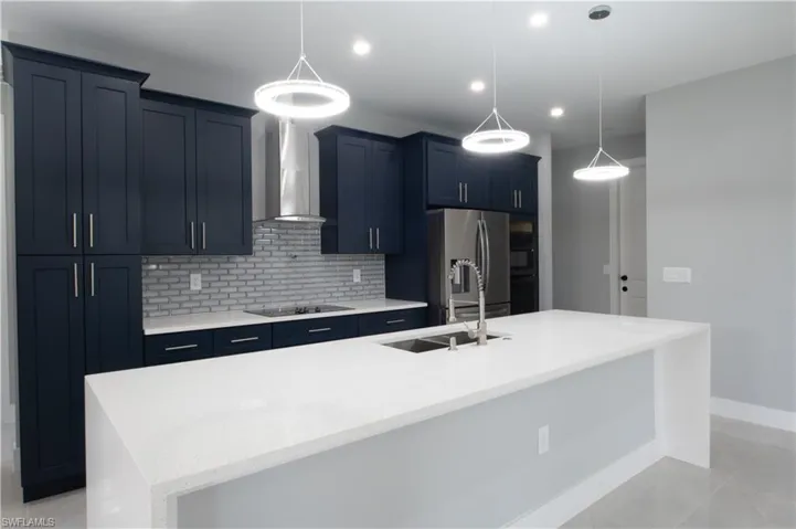 Kitchen featuring stainless steel refrigerator, sink, hanging light fixtures, a center island with sink, and wall chimney range hood