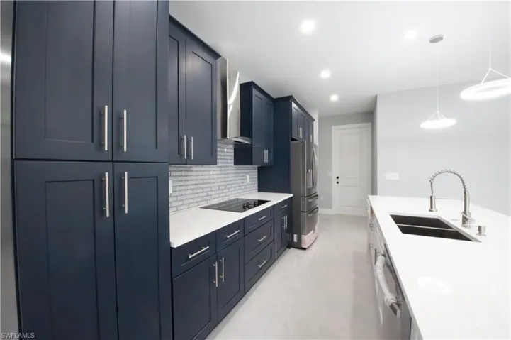 Kitchen featuring decorative light fixtures, wall chimney exhaust hood, backsplash, appliances with stainless steel finishes, and sink