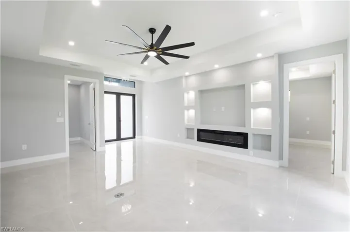 Unfurnished living room featuring a raised ceiling, ceiling fan, and light tile patterned floors