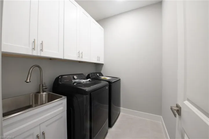 Laundry area featuring light tile patterned flooring, washing machine and clothes dryer, cabinets, and sink