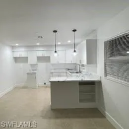 Kitchen featuring a peninsula, white cabinets, decorative light fixtures, light countertops, and recessed lighting