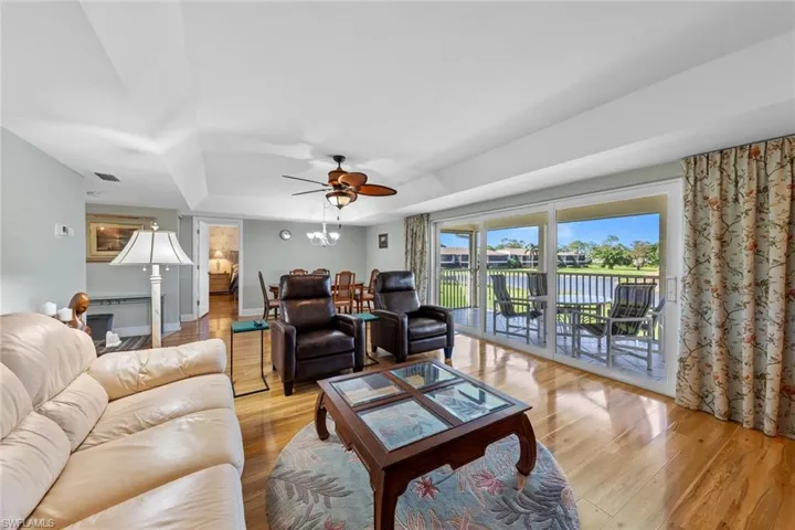 Living room with light hardwood / wood-style floors, ceiling fan, and a tray ceiling