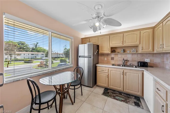 Kitchen featuring light tile patterned flooring, sink, light brown cabinets, stainless steel fridge, and decorative backsplash