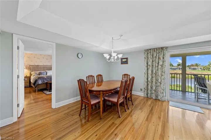 Dining space with light wood-type flooring, a water view, an inviting chandelier, and a raised ceiling