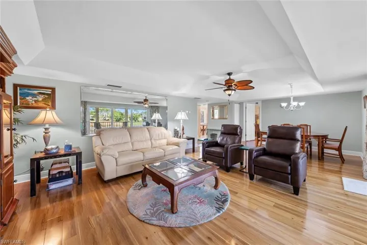 Living room with a tray ceiling, ceiling fan with notable chandelier, and light hardwood / wood-style flooring