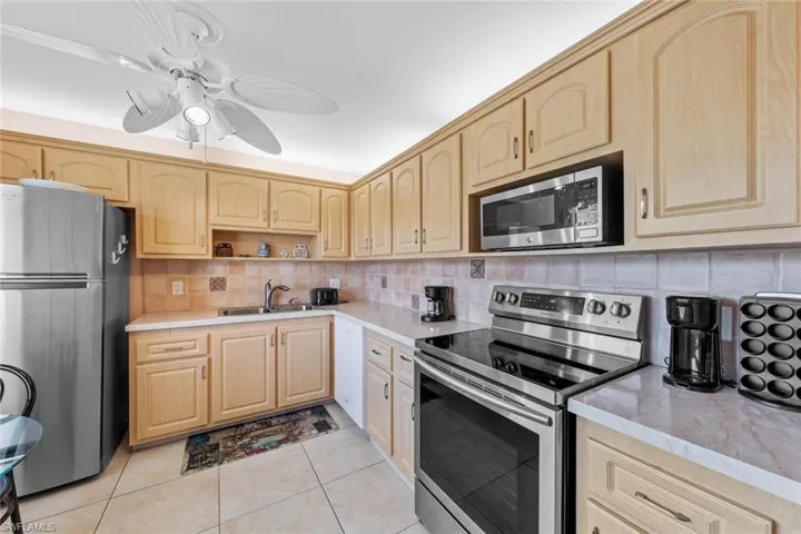 Kitchen with tasteful backsplash, light tile patterned flooring, appliances with stainless steel finishes, light brown cabinets, and sink