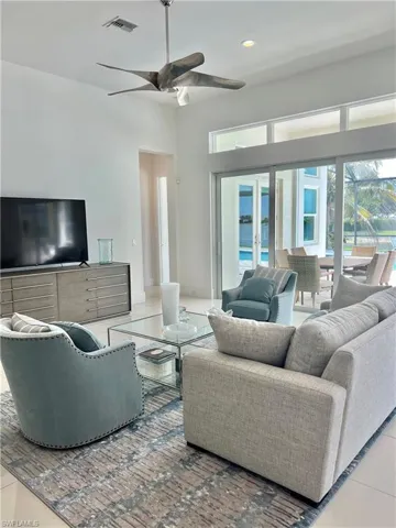 Tiled living room with ceiling fan, a towering ceiling, and a water view