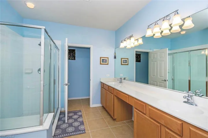 Bathroom with double vanity, a shower stall, and light tile patterned flooring