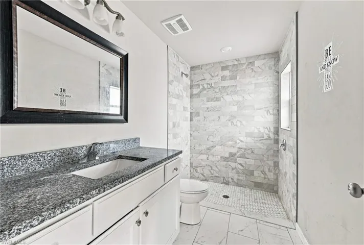 Bathroom featuring a white vanity with a granite countertop, undermount sink, and a framed mirror