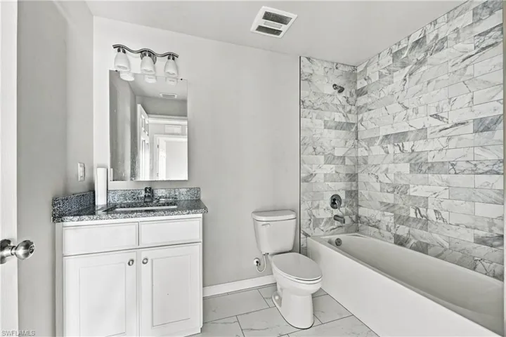 Bathroom featuring a white vanity with a dark granite-style countertop, a chrome faucet, and a wall-mounted mirror with a three-bulb light fixture