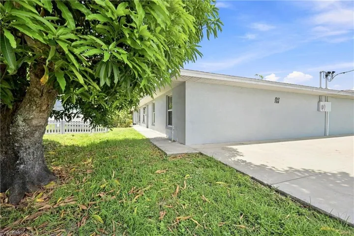 Expansive front yard with a mature tree, concrete driveway, and a white picket fence