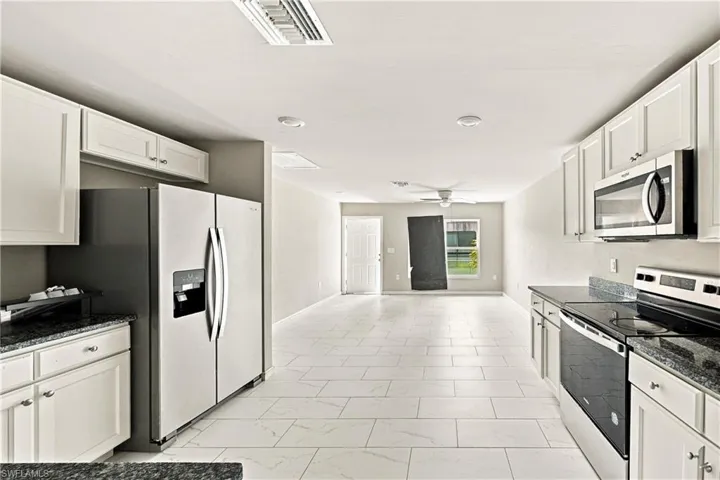 Kitchen featuring white cabinetry, stainless steel appliances, dark stone-finish countertops, and a full-height stone-finish backsplash