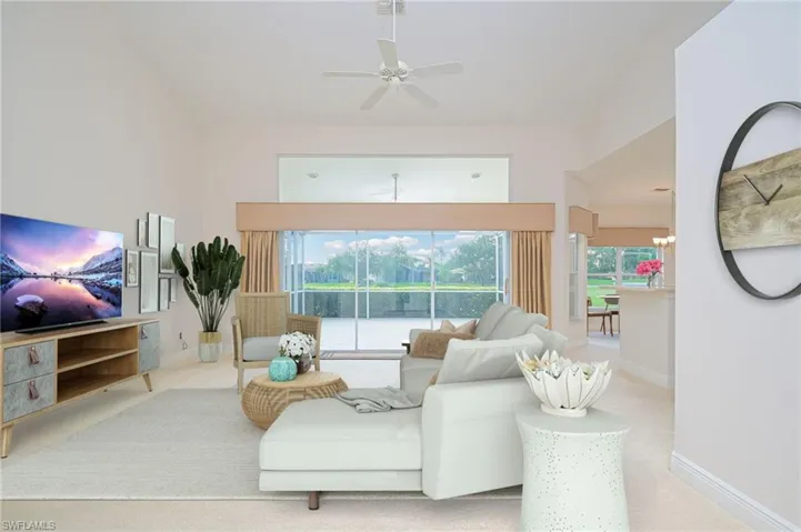 Staged Photo of living room with light carpet, a towering ceiling, and ceiling fan with notable chandelier