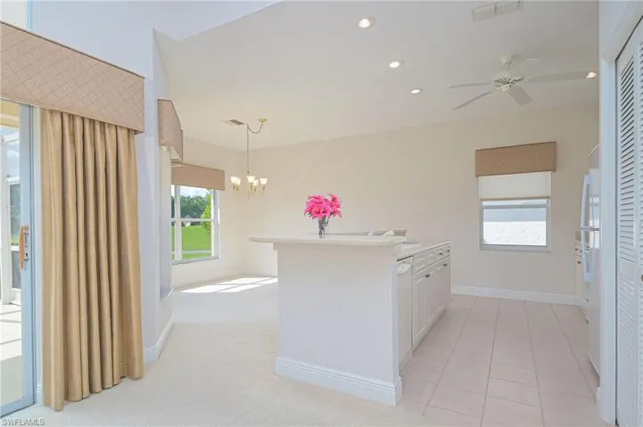 Kitchen with light carpet, white cabinetry, hanging light fixtures, and ceiling fan with notable chandelier