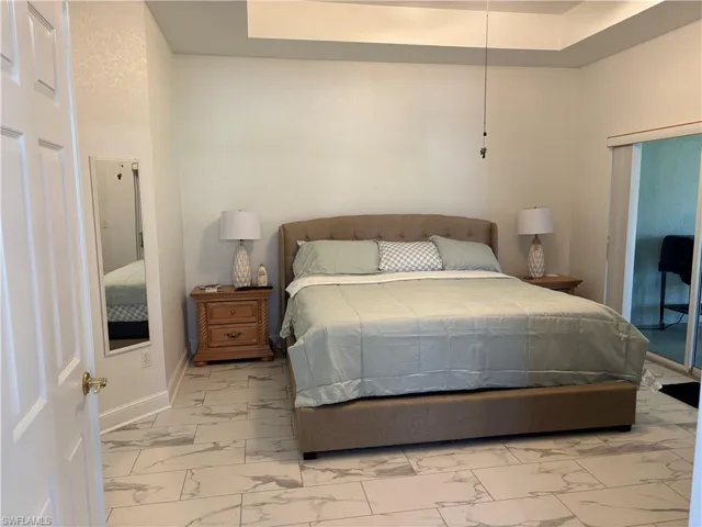 Bedroom with marble look tile flooring, a tray ceiling, and access to exterior