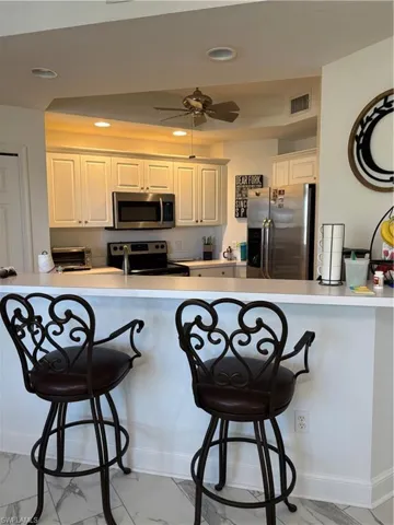 Kitchen with a kitchen breakfast bar, fridge, light countertops, light marble finish flooring, and recessed lighting