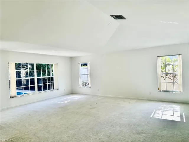 Carpeted spare room featuring vaulted ceiling and baseboards