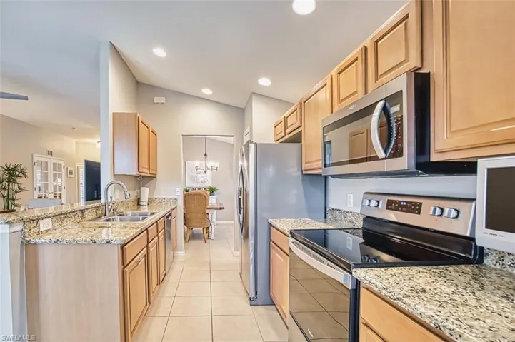 Kitchen with appliances with stainless steel finishes, light stone countertops, a chandelier, light tile patterned floors, and recessed lighting