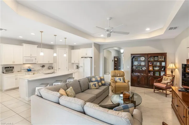 Living room featuring arched walkways, light tile patterned flooring, ceiling fan, recessed lighting, and a raised ceiling