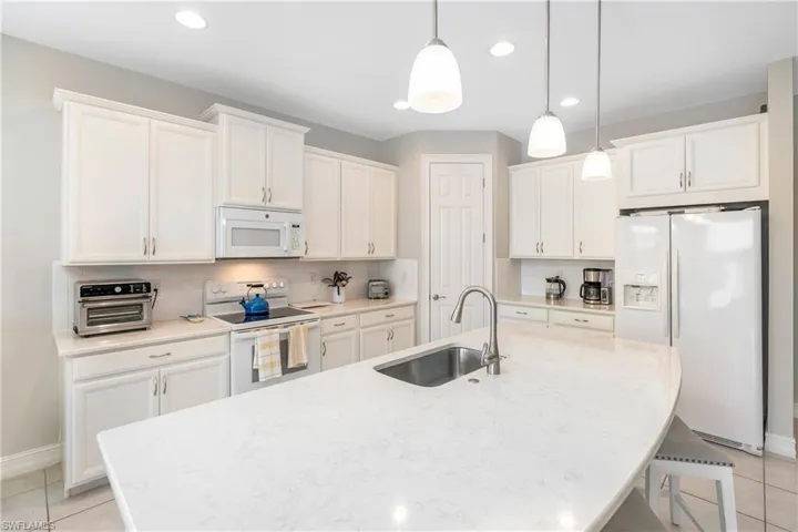 Kitchen featuring white appliances, a breakfast bar, an island with sink, white cabinetry, and recessed lighting