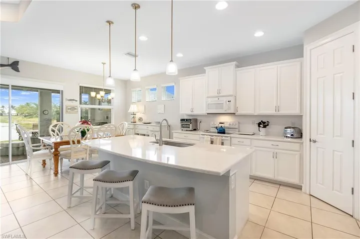 Kitchen with white appliances, healthy amount of natural light, a breakfast bar area, white cabinets, and recessed lighting