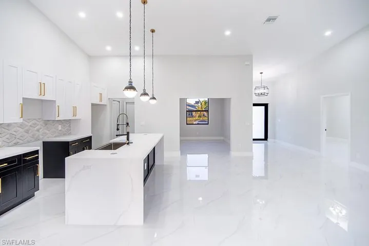 Kitchen featuring a high ceiling, two tone cabinetry, a center island with sink, light stone counters, and pendant lighting