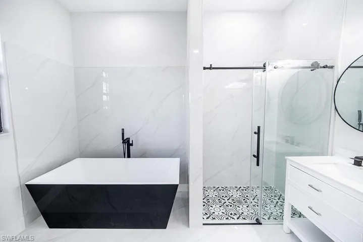 Full bath featuring vanity, a marble finish shower, and a freestanding tub