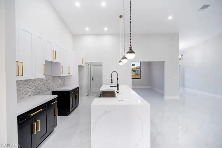 Two tone kitchen featuring two tone color scheme, hanging light fixtures, an island with sink, light stone counters, and a high ceiling