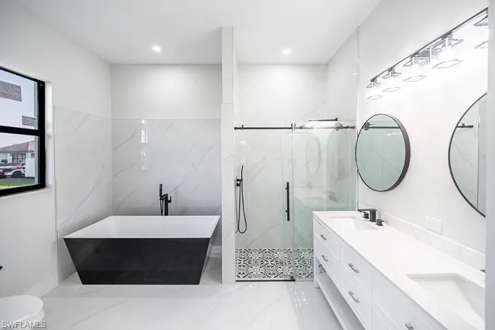 Full bathroom featuring double vanity, a soaking tub, and a marble finish shower